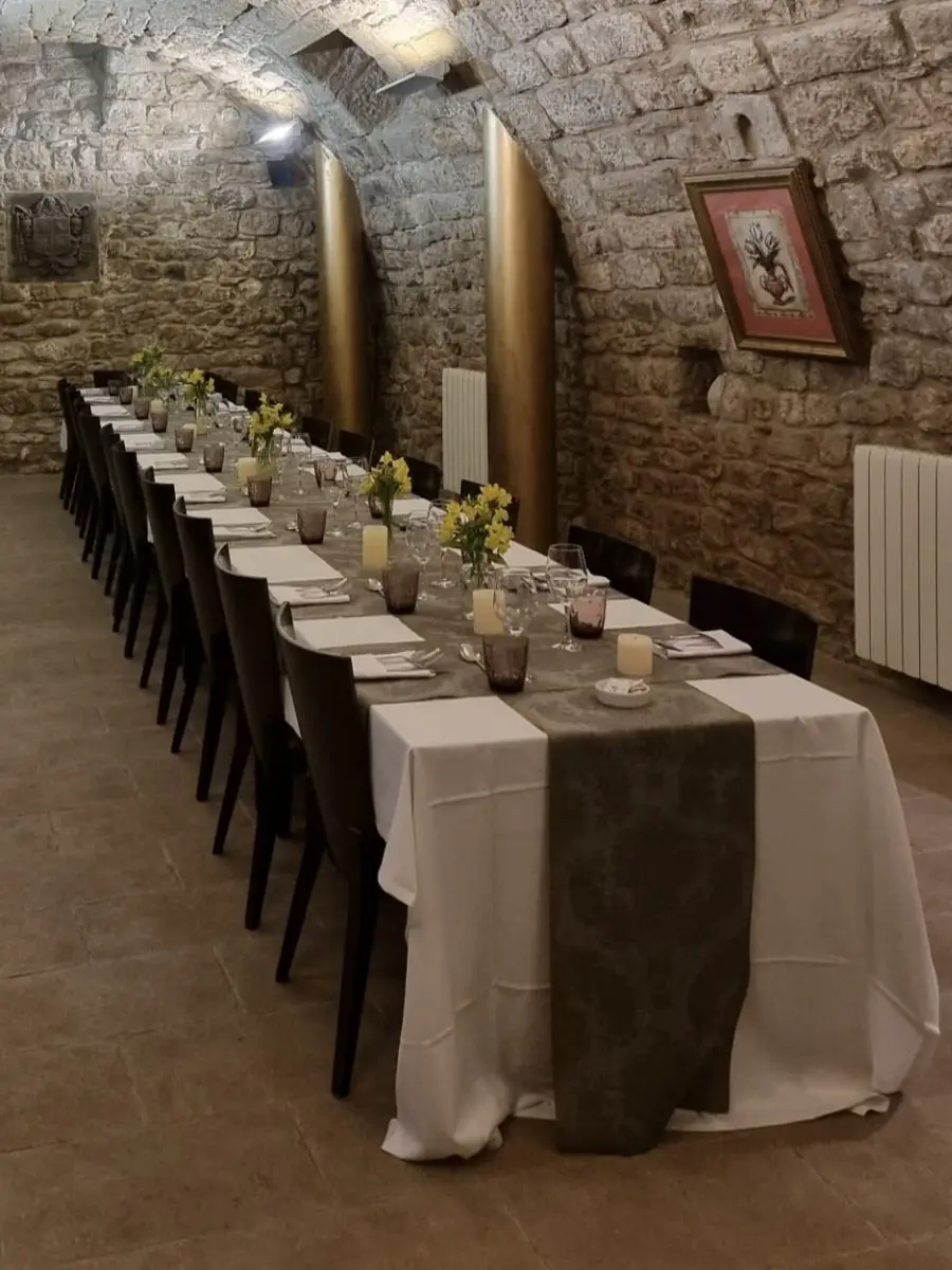 La mesa larga de la bodega, con manteles blancos, velas y flores amarillas, bajo los muros de piedra