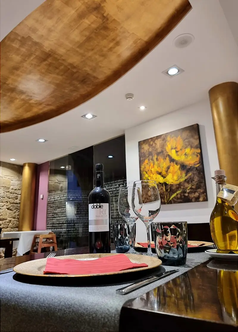 El comedor: techo dorado, columnas doradas y un cuadro de flores amarillas; en primer plano, una mesa con vino del Ribera del Duero y aceite