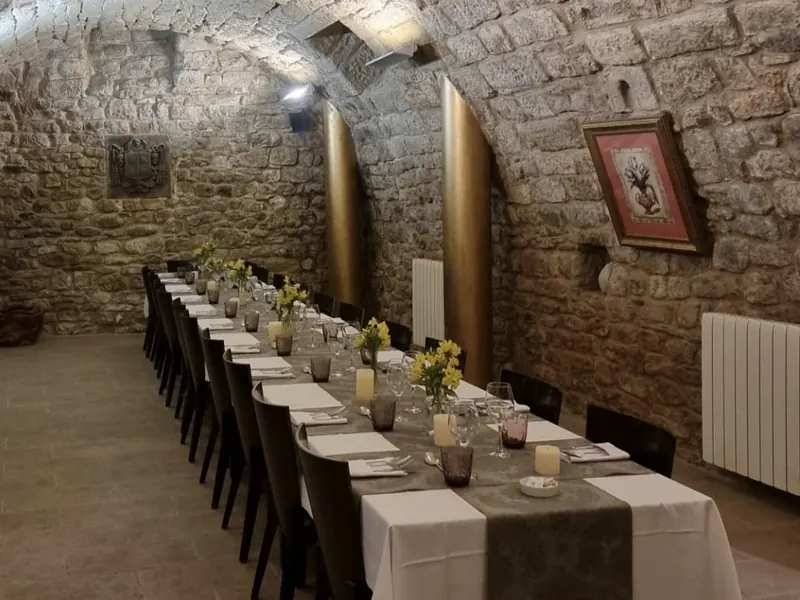 La bodega preparada para un grupo: una mesa larga con manteles blancos y flores amarillas, entre columnas doradas y bajo la bóveda de piedra