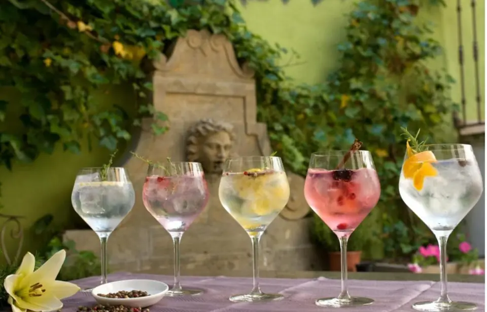 Cinco gin-tonics de colores sobre una mesa del patio, delante de una fuente de piedra con hiedra